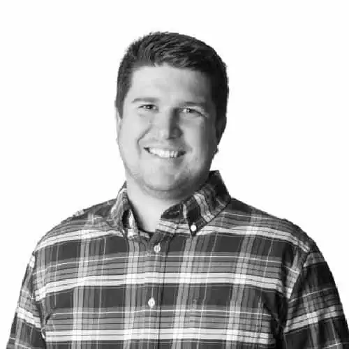  A smiling man in a checkered shirt, in a black and white portrait.