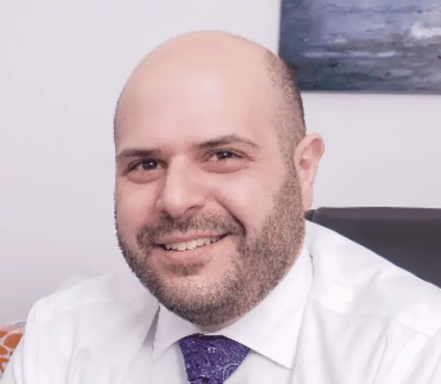  A smiling man with a neatly trimmed beard wearing a white shirt and patterned tie.